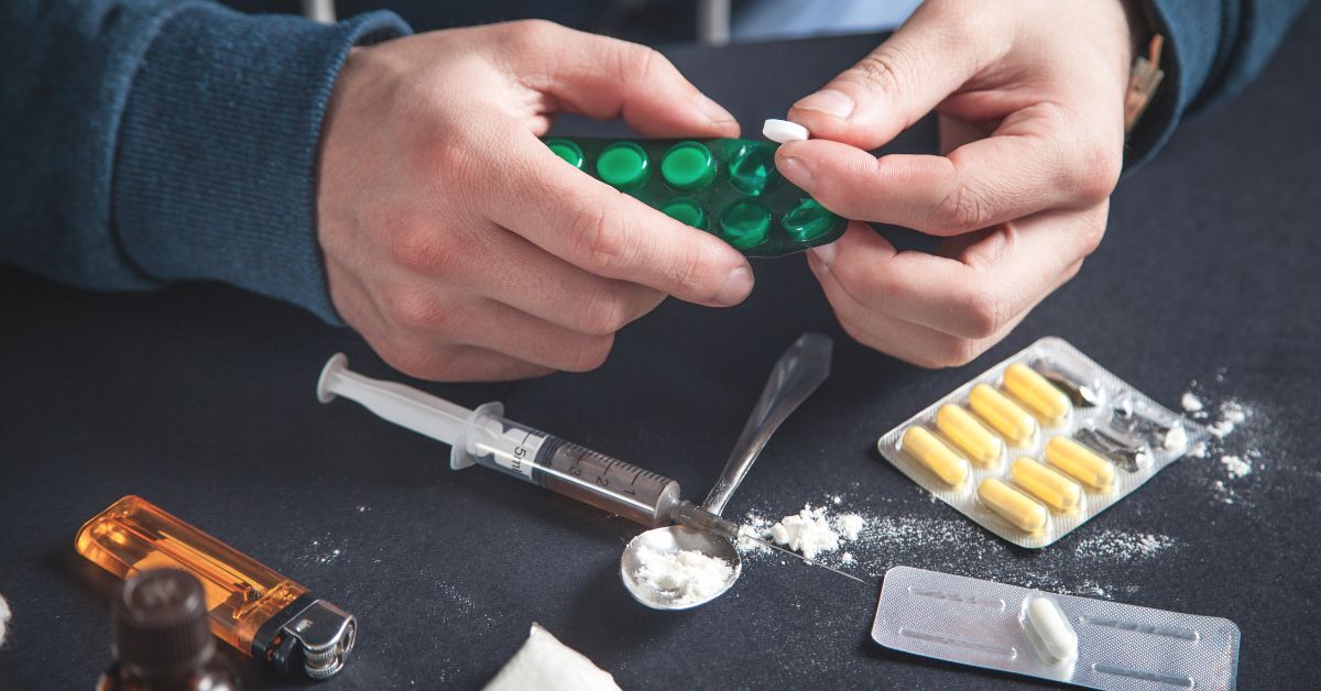 A man holding a pill and other drugs on a table, displaying warning signs of addictive personality.