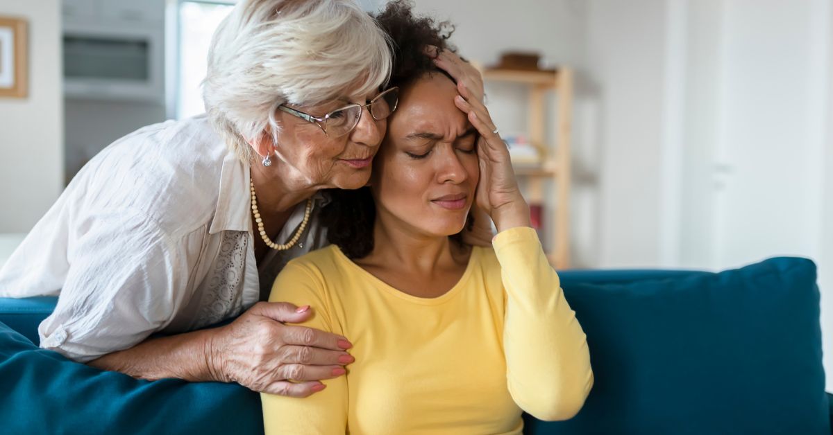 A woman is sitting on a couch with her mother thinking about the importance of patience and tolerance in recovery.